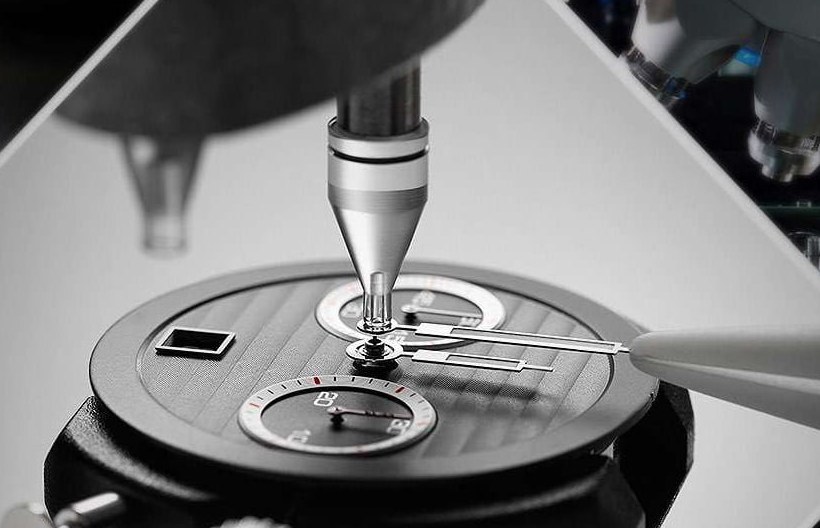 Hands being fitted to a chronograph dial under a hand setting press, photographed in black and white