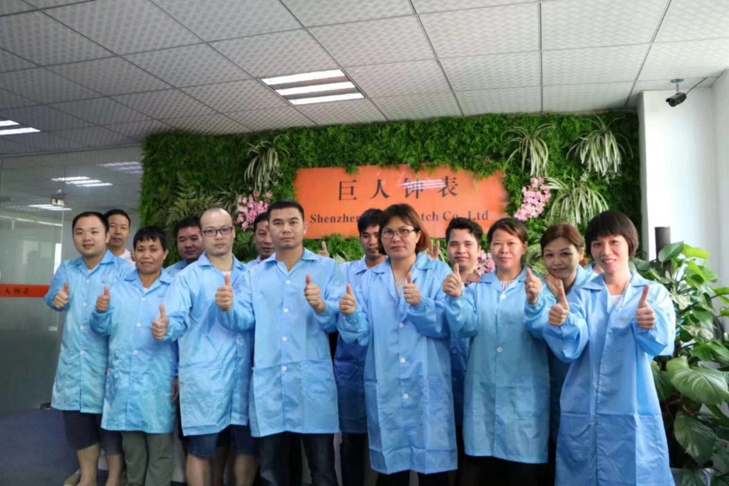 Production staff in blue coats in front of the company name board.
